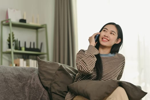 Attractive young woman chatting sharing news on mobile phone with her friend, resting in living room.