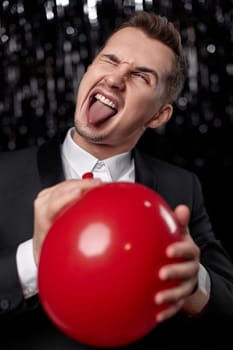 guy with red air balloon showing tongue at birthday party on dark background