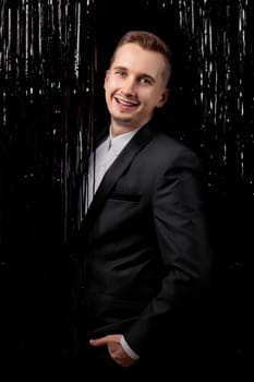 Happy handsome man in black jacket smiling on glitter background.