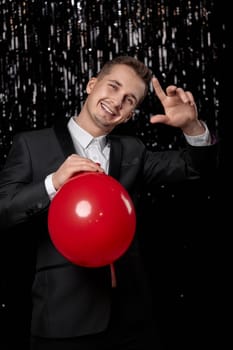 handsome man in black suit with red air balloon on dark glitter background. new year party