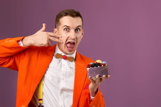 funny man in orange jacket eating cake on purple background