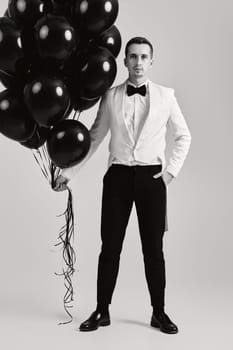 elegant caucasian man in white suit tuxedo with black air balloons on white background.