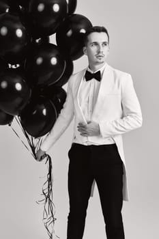 elegant guy in white suit tuxedo with black air balloons on white background. holiday celebration