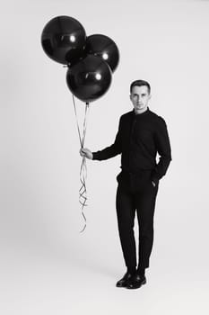 elegant caucasian man with bunch of black air balloons on white background. black and white