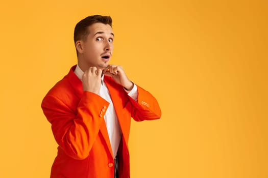 Cheerful extravagant young man in orange jacket on yellow background.