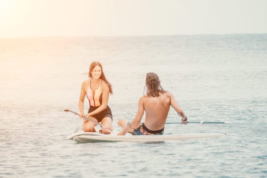 Sea woman and man on sup. Silhouette of happy young woman and man, surfing on SUP board, confident paddling through water surface. Idyllic sunset. Active lifestyle at sea or river