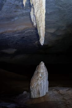 Dripping stalactite above stalagmite in dark cave