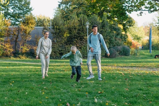 a family mom and 2 sons are having fun, running in the park and jumping. Sons, children, mom, run, play, rejoice, enjoy nature in summer. Family teamwork. Happy family team, running together in field, happily waving their hands. Group of people of different ages. happy family, mom and two sons on an emotional walk. Running and enjoying life in a green field in the park, blue sky, nature.