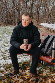 Winter Serenity: 40-Year-Old Man Enjoying Tea on Snow-Covered Bench in Rural Park. Immerse yourself in the tranquil beauty of winter as a 40-year-old man finds solace on a snowy bench in a rural park. Sipping hot tea from a thermos, he embraces the serene ambiance, surrounded by the peaceful, snow-covered nature. This captivating image captures the essence of winter leisure, offering a moment of seasonal joy and quiet contemplation amidst the breathtaking scenery.