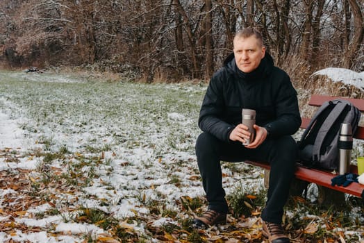 Winter Serenity: 40-Year-Old Man Enjoying Tea on Snow-Covered Bench in Rural Park. Immerse yourself in the tranquil beauty of winter as a 40-year-old man finds solace on a snowy bench in a rural park. Sipping hot tea from a thermos, he embraces the serene ambiance, surrounded by the peaceful, snow-covered nature. This captivating image captures the essence of winter leisure, offering a moment of seasonal joy and quiet contemplation amidst the breathtaking scenery.