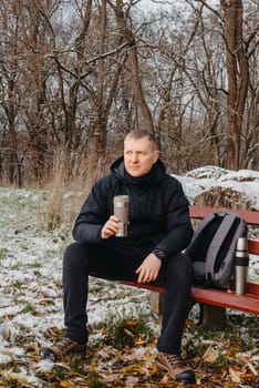 Winter Serenity: 40-Year-Old Man Enjoying Tea on Snow-Covered Bench in Rural Park. Immerse yourself in the tranquil beauty of winter as a 40-year-old man finds solace on a snowy bench in a rural park. Sipping hot tea from a thermos, he embraces the serene ambiance, surrounded by the peaceful, snow-covered nature. This captivating image captures the essence of winter leisure, offering a moment of seasonal joy and quiet contemplation amidst the breathtaking scenery.