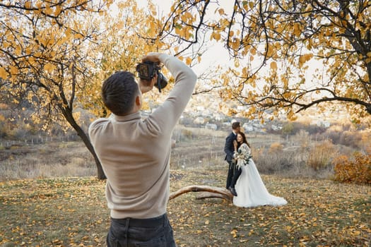 Professional wedding photographer taking pictures of the bride and groom in nature in autumn