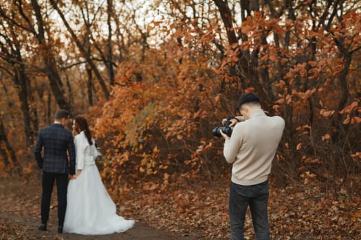 Professional wedding photographer taking pictures of the bride and groom in nature in autumn