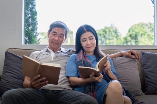 Happy elderly couple relax on couch in living room reading together for vacation holiday at home.