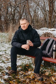 Winter Serenity: 40-Year-Old Man Enjoying Tea on Snow-Covered Bench in Rural Park. Immerse yourself in the tranquil beauty of winter as a 40-year-old man finds solace on a snowy bench in a rural park. Sipping hot tea from a thermos, he embraces the serene ambiance, surrounded by the peaceful, snow-covered nature. This captivating image captures the essence of winter leisure, offering a moment of seasonal joy and quiet contemplation amidst the breathtaking scenery.