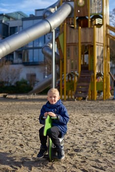 Childhood Joy: Beautiful 8-Year-Old Boy in Jacket Swinging on Horse-Shaped Seesaw, Background of Playful Park in Bietigheim-Bissingen, Germany, Autumn. Capture the pure essence of childhood happiness with this heartwarming image featuring a beautiful 8-year-old boy in a jacket, joyfully seated on a horse-shaped seesaw against the backdrop of a playful park in Bietigheim-Bissingen, Germany. The autumnal colors add warmth to this delightful scene of youthful innocence.