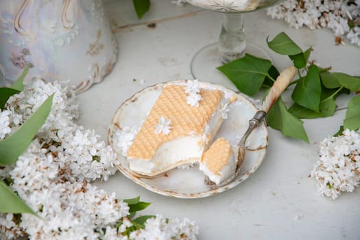 bitten waffle ice cream in a bowl and on a saucer, spring still life with a bouquet of white lilacs, antique porcelain tableware, romantic break for dessert, high quality photo