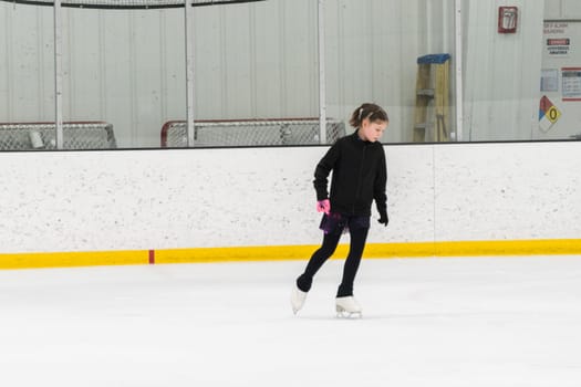 Young girl perfecting her figure skating routine while wearing her competition dress at an indoor ice rink.