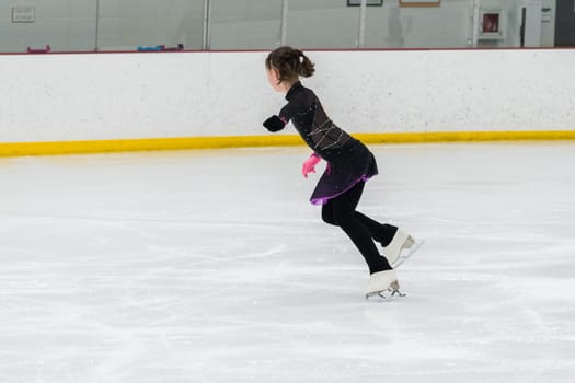 Young girl perfecting her figure skating routine while wearing her competition dress at an indoor ice rink.