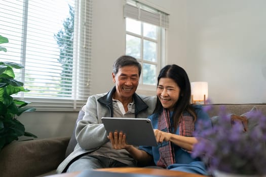 Retired elderly couple sits on couch using tablet together and relax in their home. Senior Activity Concept.