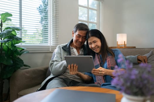 Retired elderly couple sits on couch using tablet together and relax in their home. Senior Activity Concept.