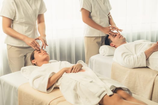 Caucasian couple enjoying relaxing anti-stress head massage and pampering facial beauty skin recreation leisure in dayspa modern light ambient at luxury resort or hotel spa salon. Quiescent