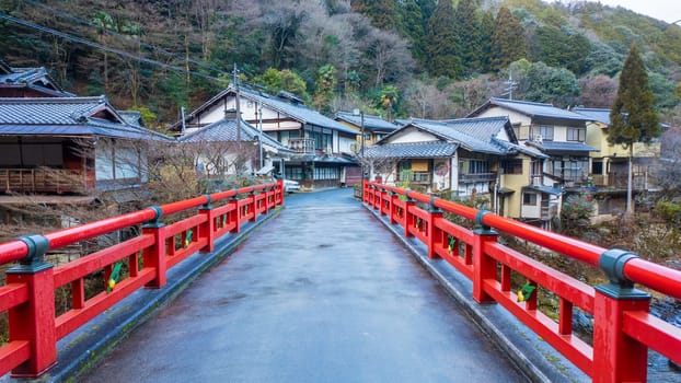 Narrow red bridge leads to traditional houses in Japanese village. High quality photo
