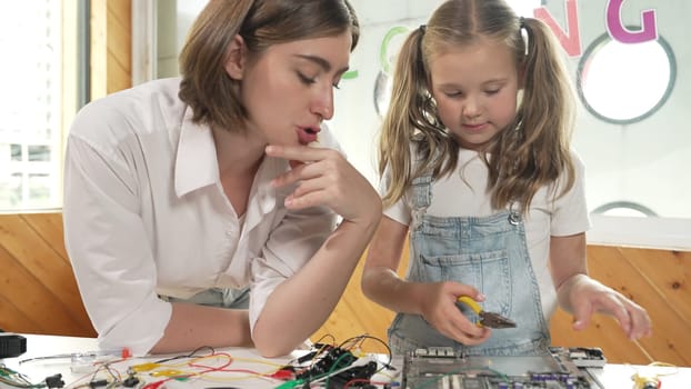 Young smart caucasian teacher teaching students about part of electronic board. Expert girl learn about digital electrical tool and fixing motherboard at table with chips and wires placed. Erudition.