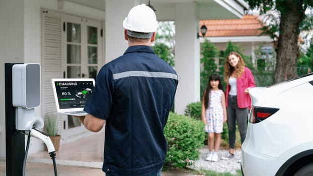 Qualified technician work on home EV charging station installation, make troubleshooting and configuration setup on charging system with laptop for EV at home with family present. Panorama Synchronos