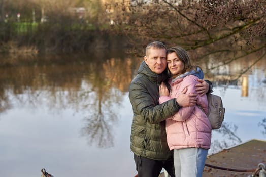 Loving couple sit on the shore of the pond in the park in autumn. A man and a woman. A couple, lovers on the shore of the lake on a walk