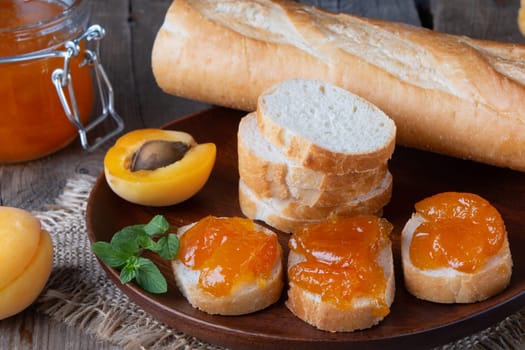 Toasts of bread with apricot jam and fresh fruits with mint on wooden table. Tasty breakfast.