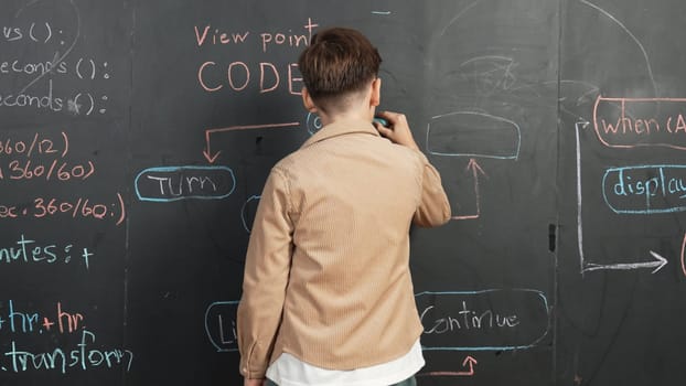 Back view of smart boy writing engineering prompt on blackboard. Attractive happy student planing a project by using coding and programing system in STEM technology classroom. Closeup. Erudition.