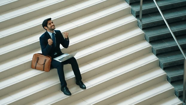 Top view business man celebrate successful project while sitting at stairs. Smart project manager getting new gob, getting promotion, increasing sales while calling friends by using laptop. Exultant.