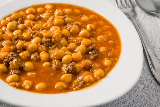 Chickpea stew with minced meat on a white porcelain plate on a stone table