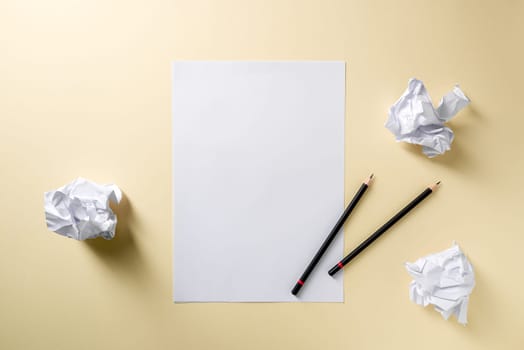 Blank writing sheet with pen and crumpled paper balls lay flat on yellow background
