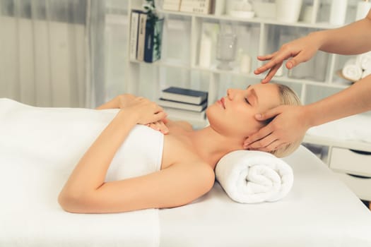 Caucasian woman enjoying relaxing anti-stress head massage and pampering facial beauty skin recreation leisure in dayspa modern light ambient at luxury resort or hotel spa salon. Quiescent