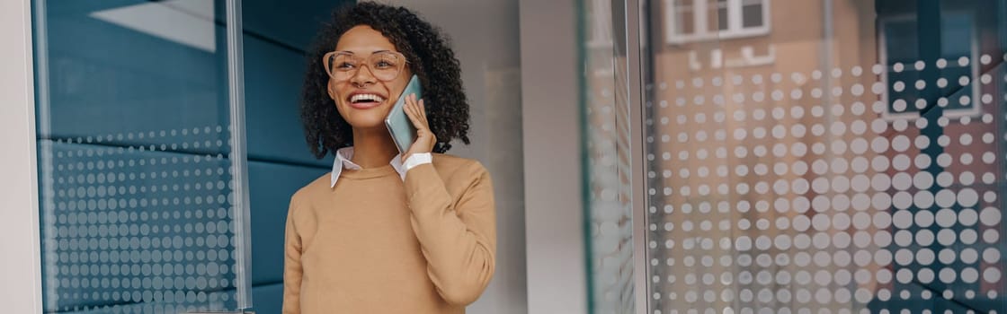 Stylish female freelancer is talking phone while standing on coworking background