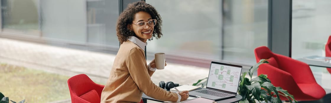 Smiling female freelancer have coffee break during working on laptop in modern coworking