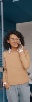 Smiling businesswoman is talking phone with client while standing on modern office background