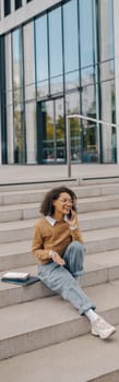 Smiling female freelancer talking phone with client while sitting on building background