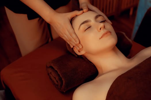 Caucasian woman enjoying relaxing anti-stress head massage and pampering facial beauty skin recreation leisure in warm candle lighting ambient salon spa in luxury resort or hotel. Quiescent