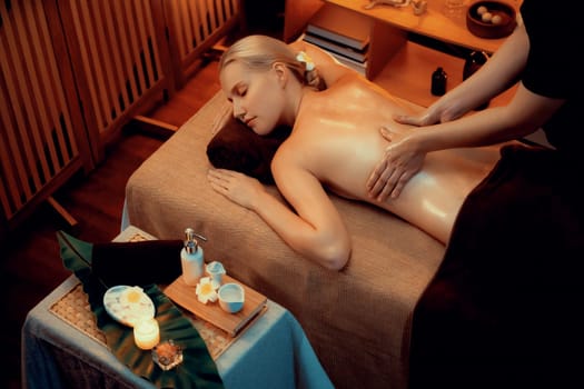 Caucasian woman customer enjoying relaxing anti-stress spa massage and pampering with beauty skin recreation leisure in warm candle lighting ambient salon spa at luxury resort or hotel. Quiescent