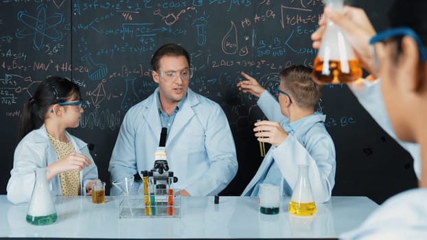 Smart teacher explain about chemical theory while student mixing colored solution or doing experiment. Instructor teaching chemistry while pointing at blackboard in STEM science class. Edification.