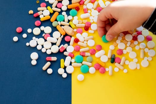 Top view of child hand holding tablet pills against yellow background. Many tablets, pills, medicines