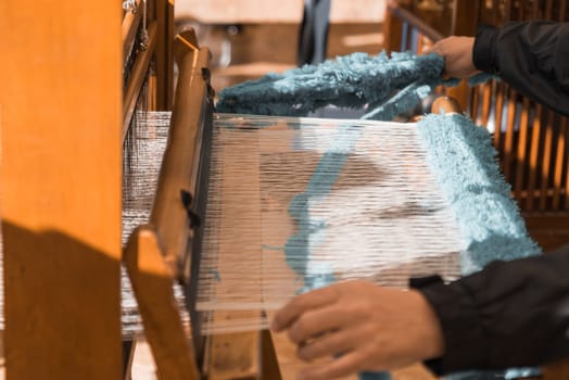 Master weaver is weaving the tapestry with diverse bright threads, close up. Artisanal at work.