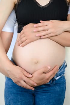 Bare belly of a pregnant woman, a married couple is waiting for the birth of their child, hands on the belly of a pregnant woman.