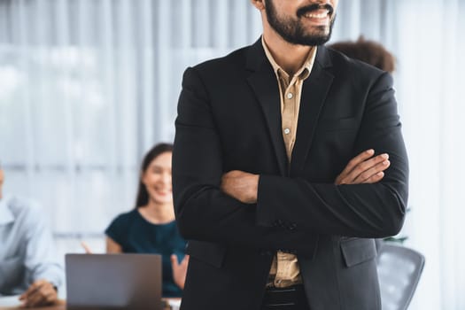 Businessman poses confidently with diverse coworkers in busy meeting room background. Multicultural team works together for business success. Modern businessman portrait. Concord