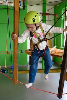 A little girl is walking on a cablewaya playroom with a cable car, a helmet and a belay is worn by a girl while running on a cable car.