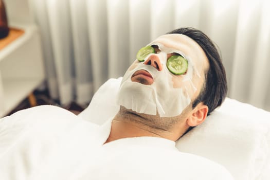 Serene daylight ambiance of spa salon, man customer indulges in rejuvenating with luxurious cucumber facial mask. Facial skincare treatment and beauty care concept. Quiescent