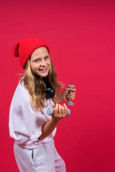 Kid girl doing fitness exercises with dumbbells on a red background